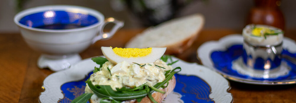 Veganes Sonntagsfrühstück: veganes hartes Ei auf veganem Eiersalat auf einem Brötchen. Dazu ein hartgekochtes Ei mit Salz, Pfeffer und Schnittlauch und natürlich eine Tasse Kaffee.