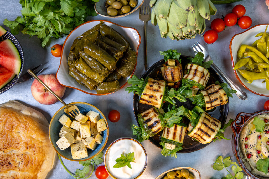 Gefüllte Weinblätter mit gegrillten Zucchini, Veta, Baba Ganoush, Joghurt-Dip, Obst und Gemüse auf einem reichhaltigen Tisch voller Mezze