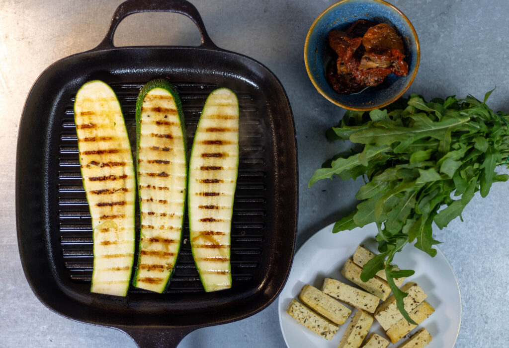 3. Die Zucchiniescheiben werden in der Grillpfanne gegrillt. Daneben die Zutaten für die Füllung der Röllchen.