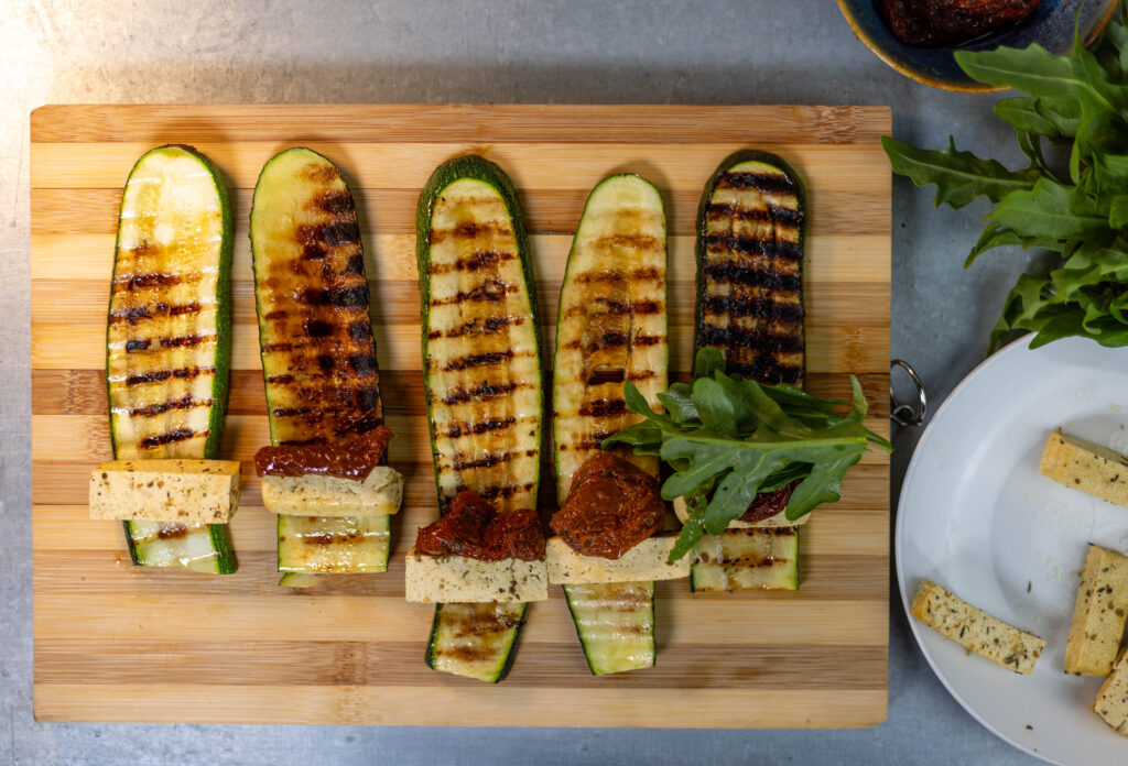 4. Ein Ende der grgrillten Zucchinistreifen mit der Füllung aus Veta, getrockneter Tomate und Rucola belegen.