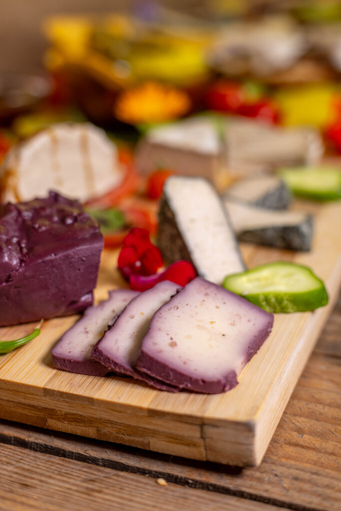 Echte Genießer*innen geben ihrem veganen Käse Zeit. Hier sieht man meinen Kartoffelkäse in Rotwein gereift. Im Hintergrund: veganer Mozzarella, gereifter Käse mit Weiß- und Blauschimmelkulturen, sowie diverse weiere vegane Käsesorten