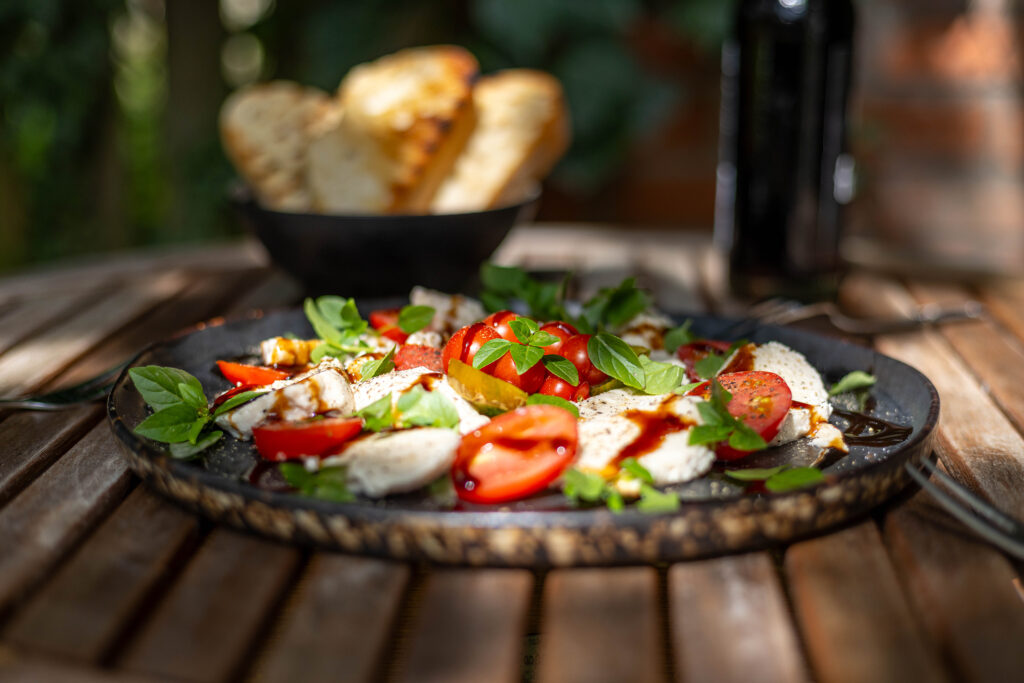 Veganer Mozzarella Caprese im Garten mit selbstgezogenen Tomaten und Basilikum.