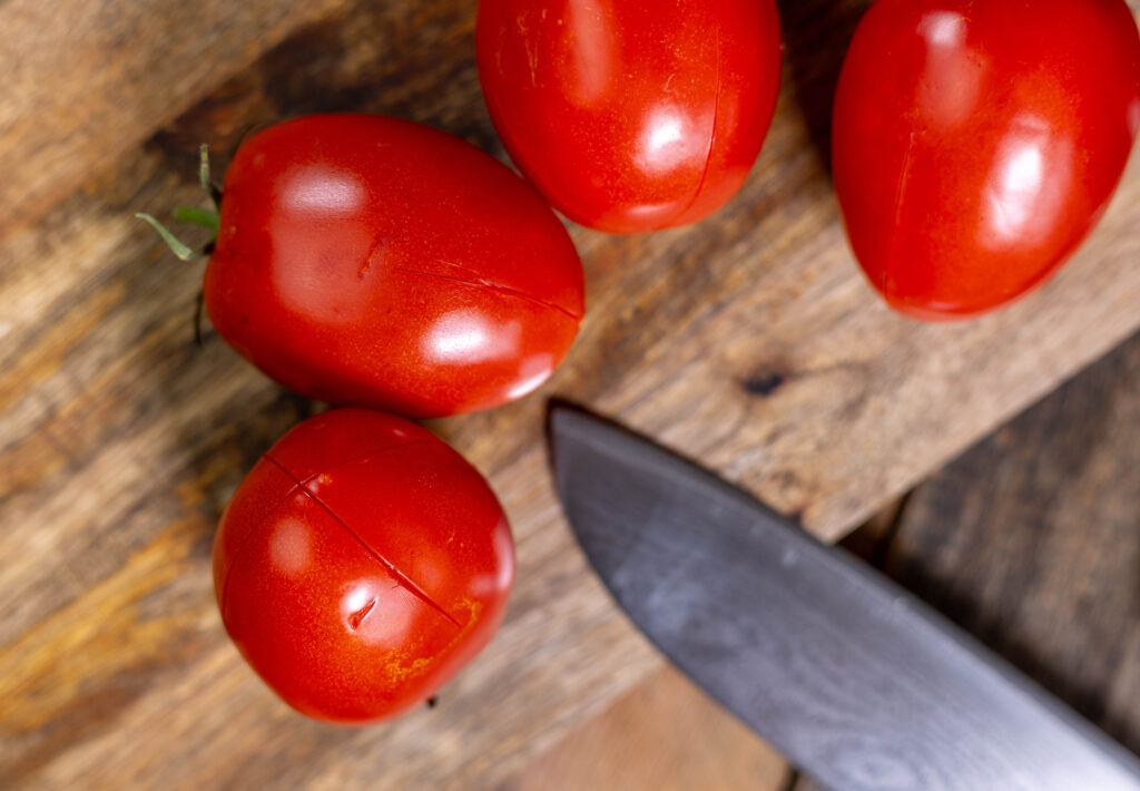 2. Die Tomaten kreuzförmig an der Unterseite einritzen, dann kurz in heißem Wasser blanchieren.