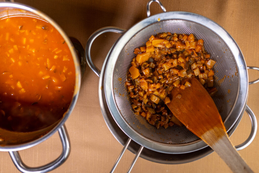 7. Die Sauce durch ein Sieb passieren. Dabei die Genmüsestücke kräftig in das Sieb drücken. Es soll möglichst viel Gemüse durch das Sieb gepresst werden. Das macht die Bratensauce sämiger und aromatischer. Zum Schluss erneut aufkochen und mit Salz und Pfeffer abschmecken.