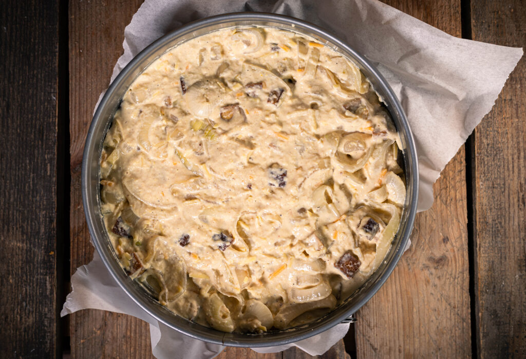 8. Die Rohmasse für den bodenlosen Zwiebelkuchen wird in der Backform glatt gestrichen. Dann kommt er in den Ofen.