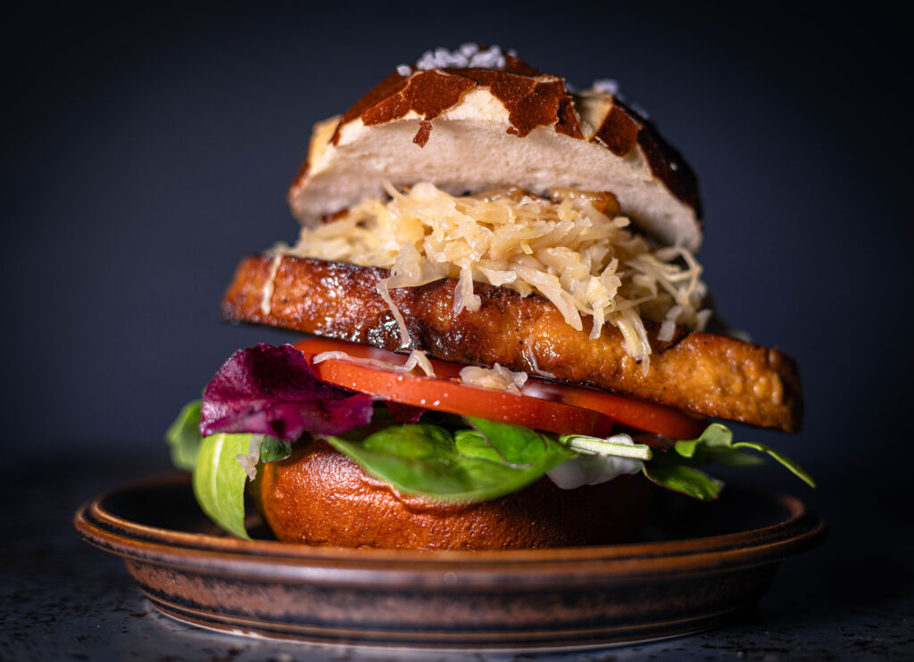 Saftig-rauchiges, gebratenes Kassler mit Sauerkraut, zweierlei Senf und Schmelzzwiebeln auf einem weichen Laugen-Bun.