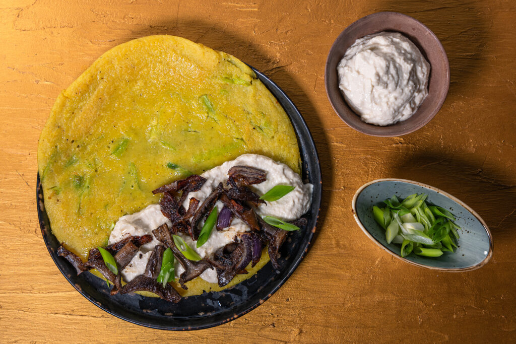 6. Das Omelette auf einen Teller geben und mit veganem Ricotta, den gebratenen Waldpilzen und Lauchzwiebelringen füllen.