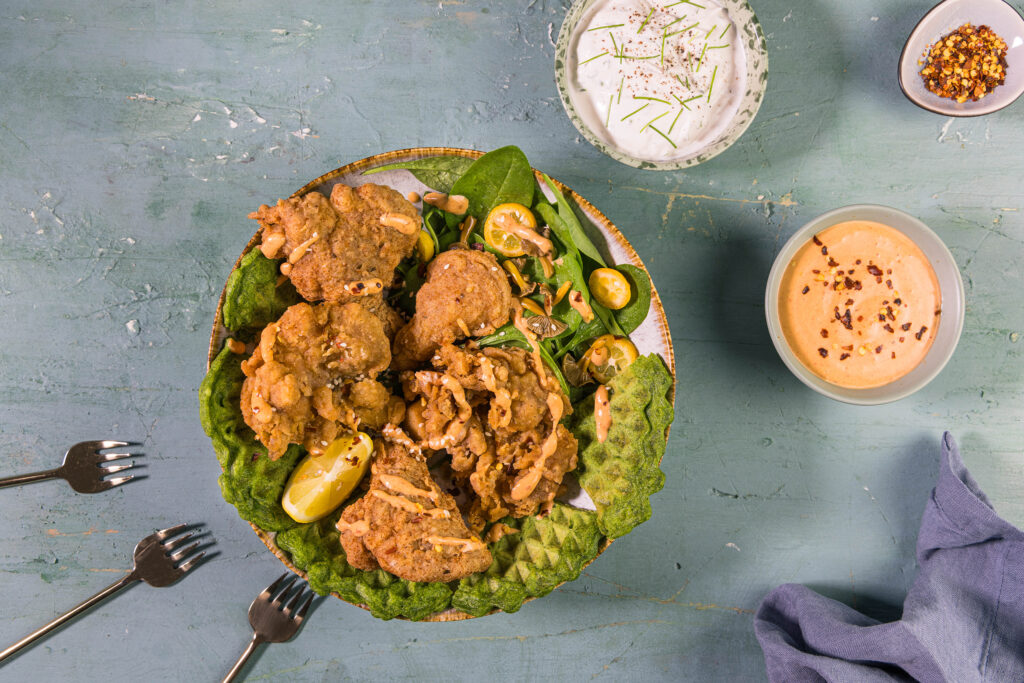 Vegane Austernseitling Nuggets mit zwei Dips, Chiliflocken und drei Gabeln auf einem grünen, alten Tisch