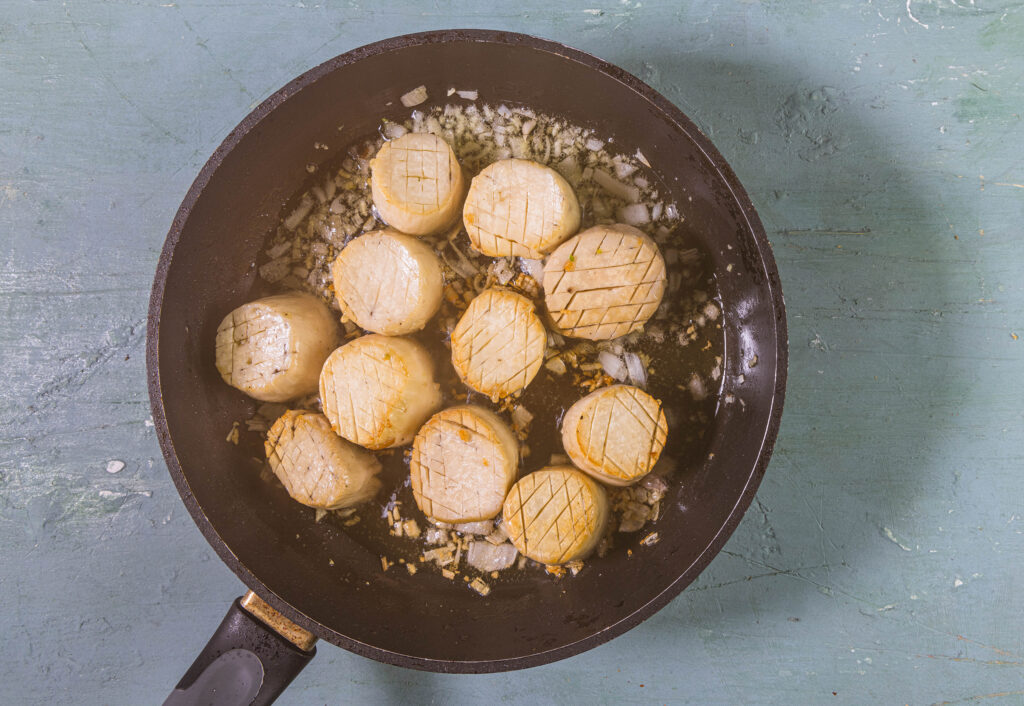 Die veganen Jakobsmuscheln werden in den Zwiebeln und Schalotten in einer Pfanne angebraten.