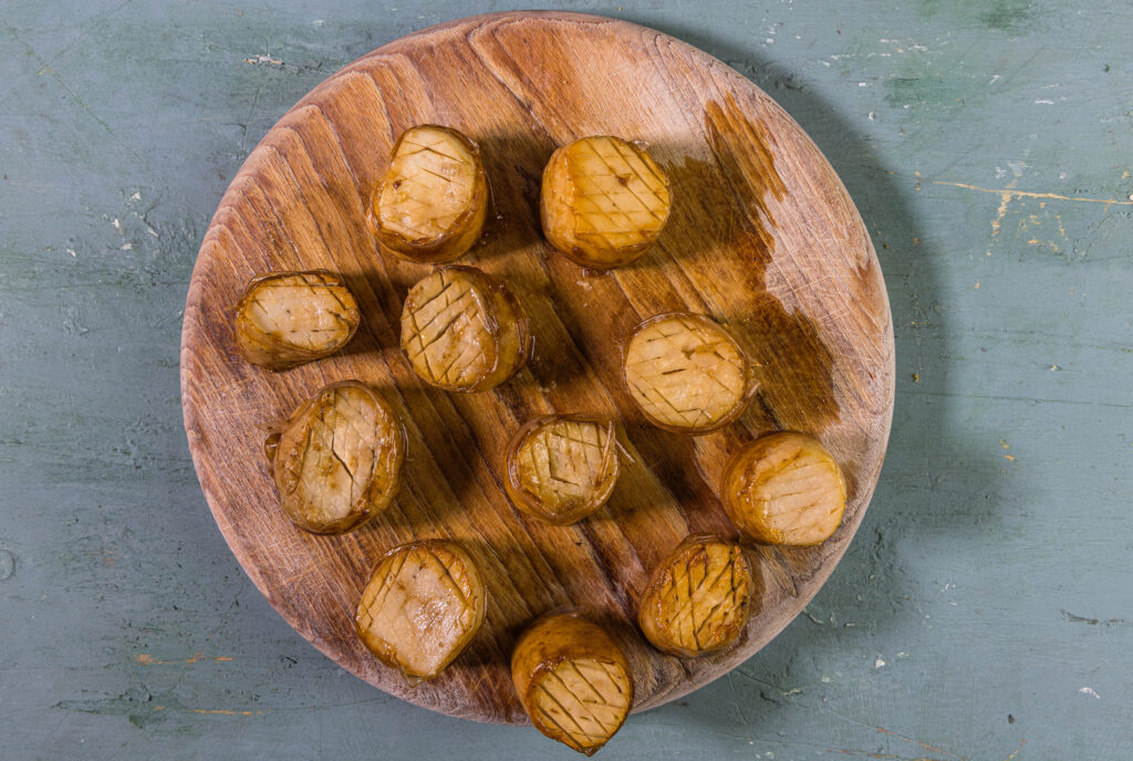 Die veganen Jakobsmuschlen, umwickelt mit Reispapierstreifen, auf einem Holzbrett.