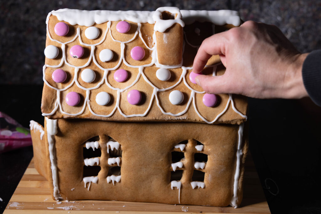 12. Mit Zuckerguss klebe ich vegane Schokolinsen auf das Hexenhaus.