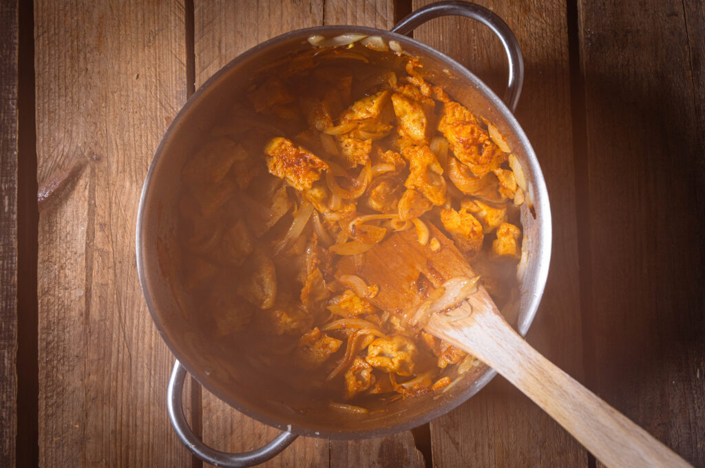 Seitanstücke braten mit verschiedenen Gewürzen und Zwiebeln im Topf.