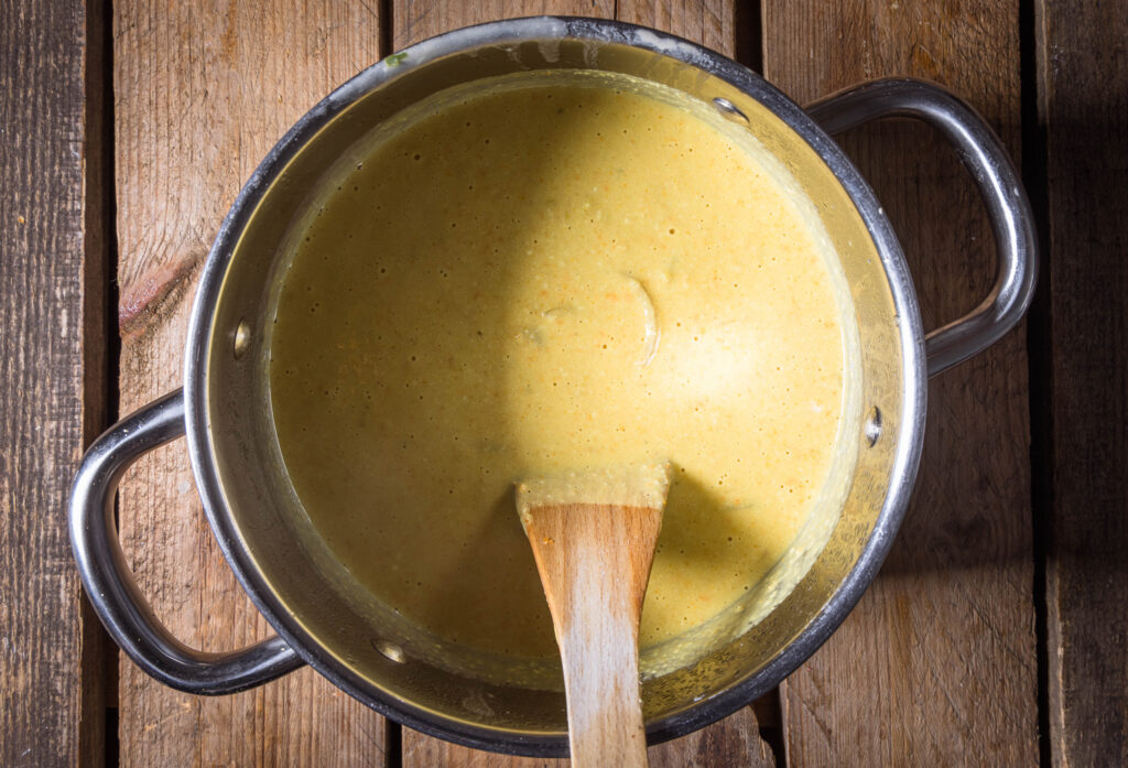 Vegane Fonduesuppe in einem Kochtopf mit Kochlöffel.