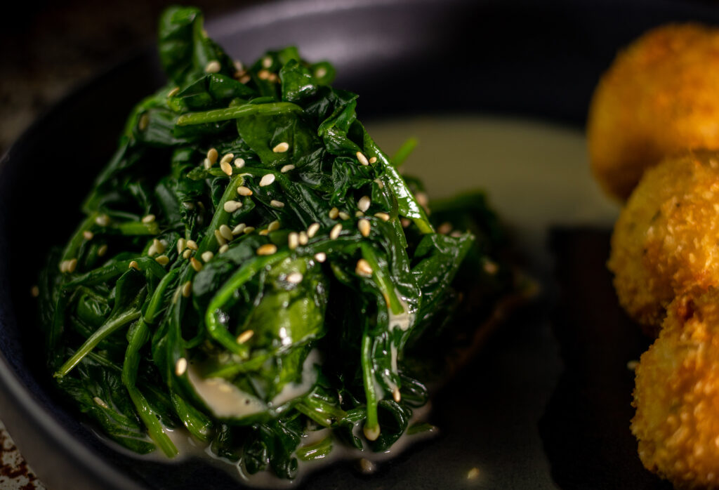 Spinach-sesame salad on a plate with vegan, fired mozzarella balls