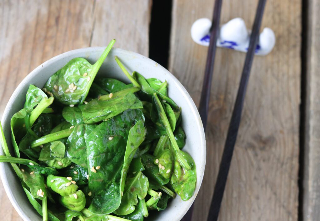 Spinach-sesame-salad in a bowl on a wooden table with chop sticks.