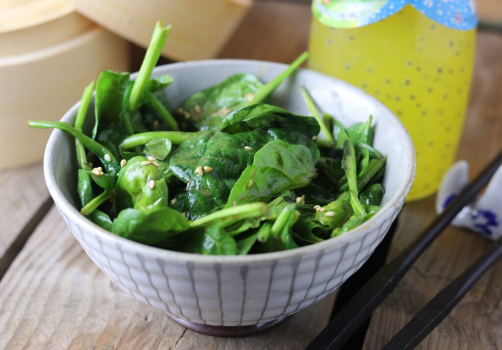 Japanese spinach and sesame salad on a wooden table with chop sticks and a drink