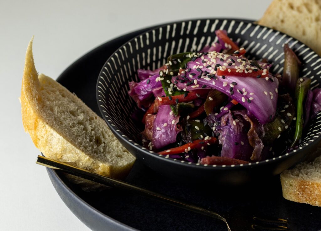 Vegan kimchi in a bowl on a plate with bread.