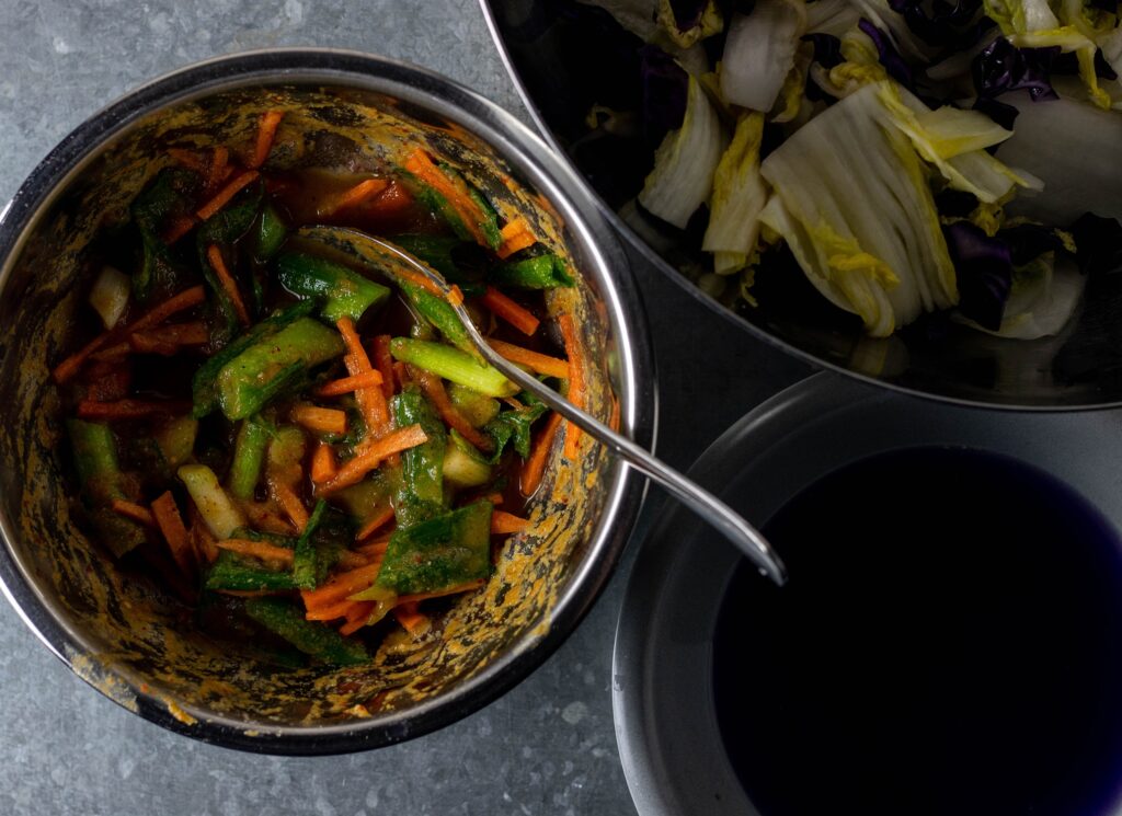 Vvegetables are partially added to a seasoning paste in a bowl.