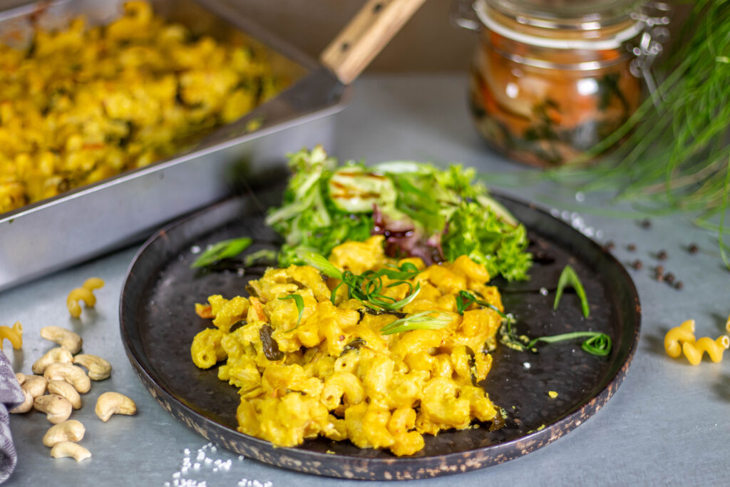 A plate with vegan kimchi mac and cheese as well as a salad on the side. Kimchi and more mac and cheese in the background.