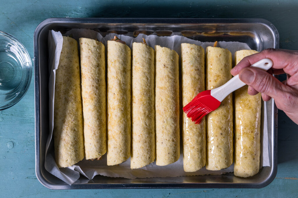 Vegane Taquitos werden in einer Auflaufform mit etwas Öl bepinselt.