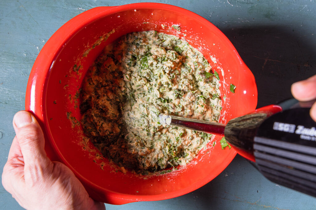 Eine Schüssel von oben, darin ein Pürierstab und ein bisher nur grob pürierter Hummus.