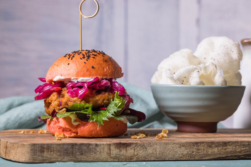 Vegane Kimchi-Burger auf einem Holzbrett. Mit veganen Krupuk als Beilage in einer Schale.