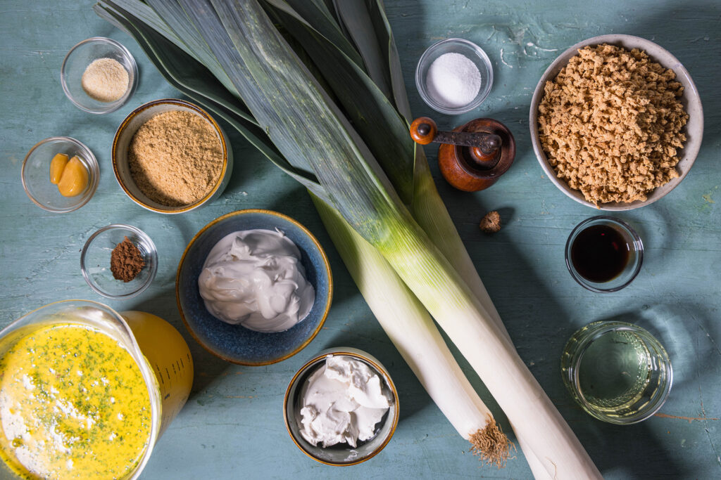 Alle Zutaten für die veganen Lauch-Hack-Käse-Suppe auf einem alten, grünlichen Tisch.