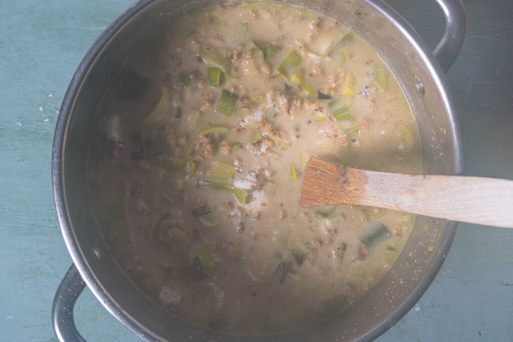 Dampfende, vegane Lauch-Käse-Hack-Suppe in einem Kochtopf mit Kochlöffel.