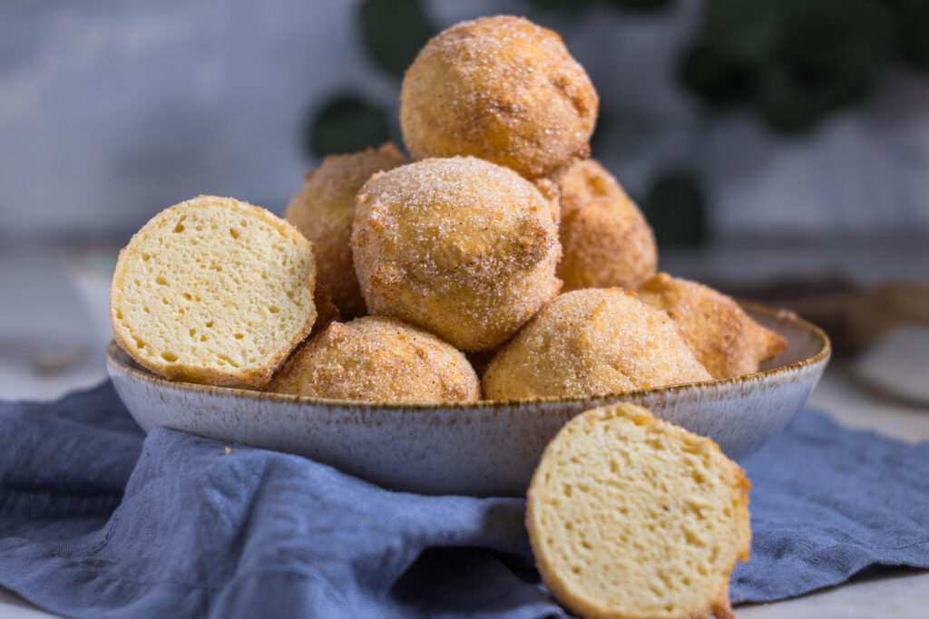 Vegane Quarkbällchen in einer Schüssel. Einer ist aufgeschnitten. Die zarte, luftige Krume des Teigs zeigt in die Kamera.