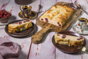 Frisch gebackener, veganer Quarkstrudel mit Kirschen und Blätterteig mit Esspressotassen auf einer Kaffeetafel.