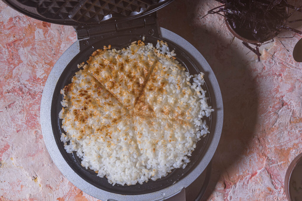 Ein Waffeleisen, geöffnet. Man sieht eine knusprig-braune Sushiwaffel darin.