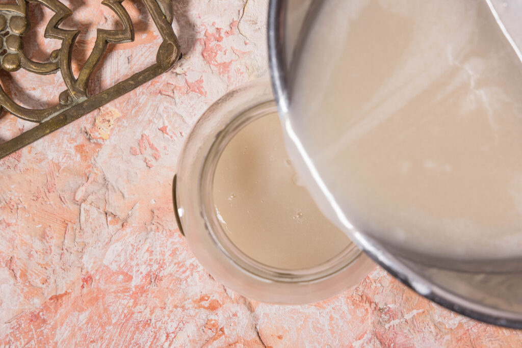 Kondensmilch wird aus einem Topf in ein Glas abgefüllt.