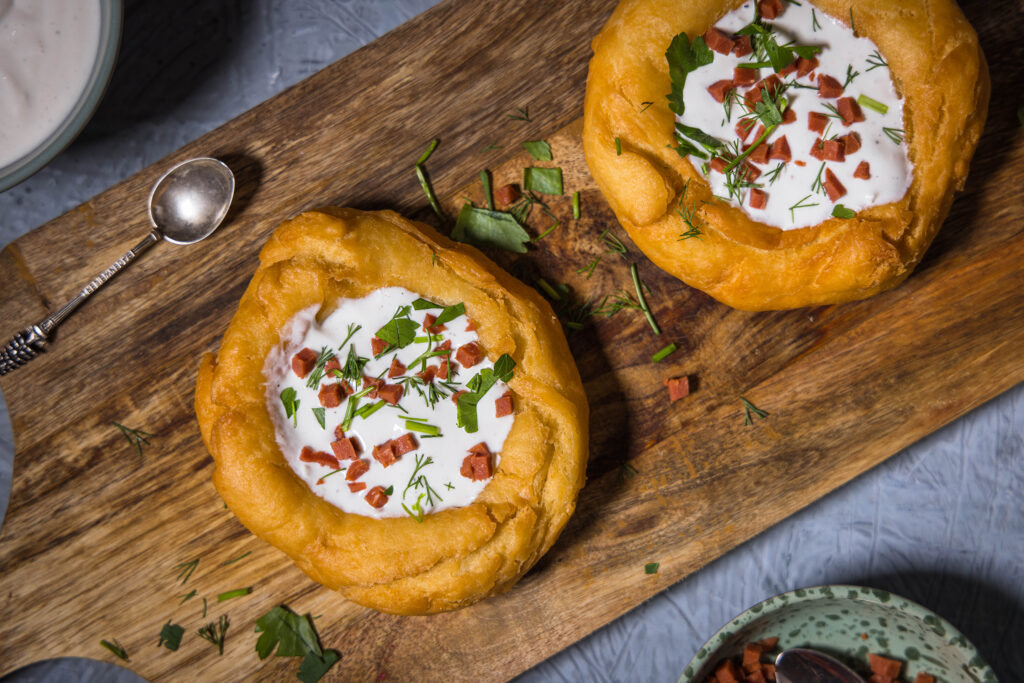 2 vegane Lángos auf einem Holzbrett. Davor und dahinter kleine Schalen mit Toppings.