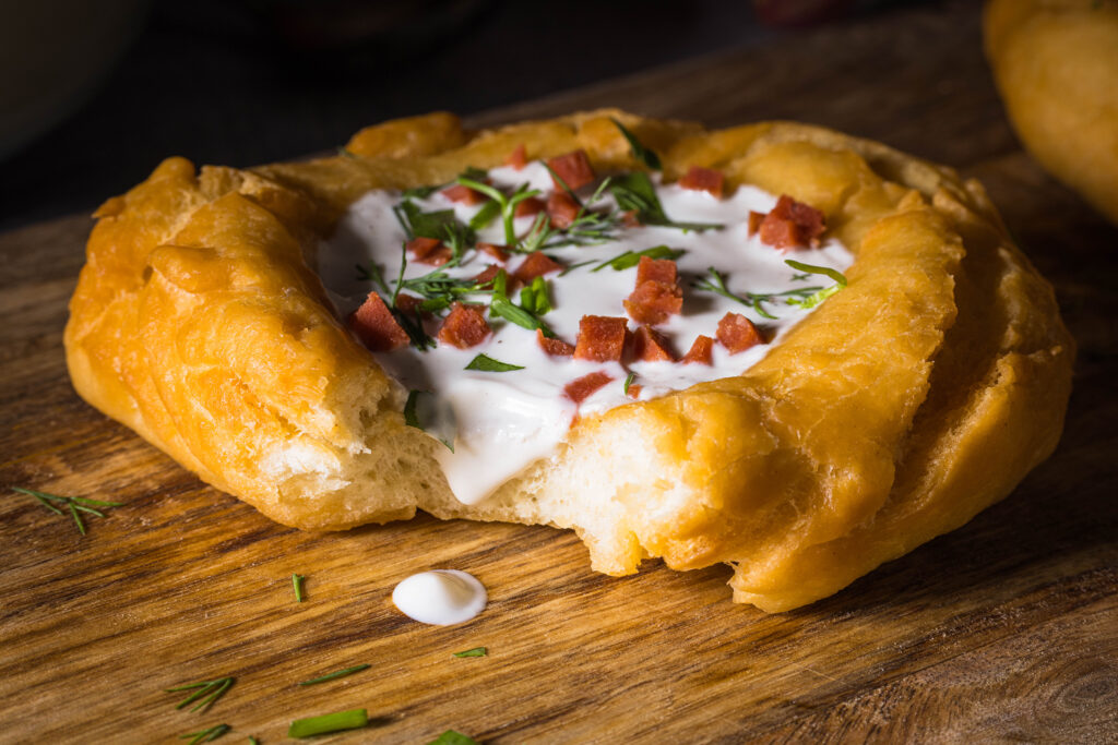 Lángos mit einer Knoblauchcreme aus Sauerrahm belegt auf einem Holzbrett. Hier vegan.