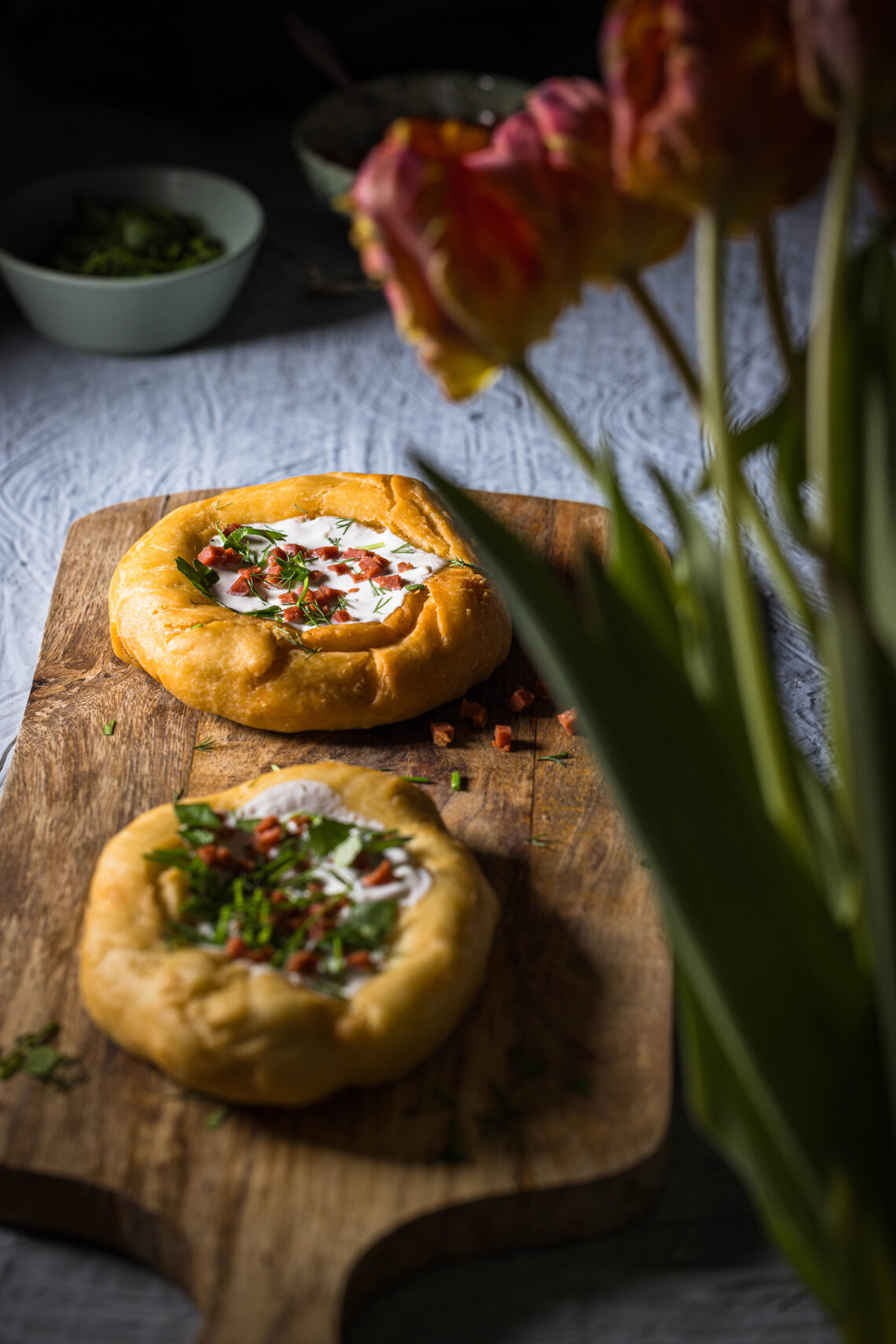 2 vegane Lángos auf einem Holzbrett. Davor ein Strauss Tulpen. Dahinter kleine Schalen.