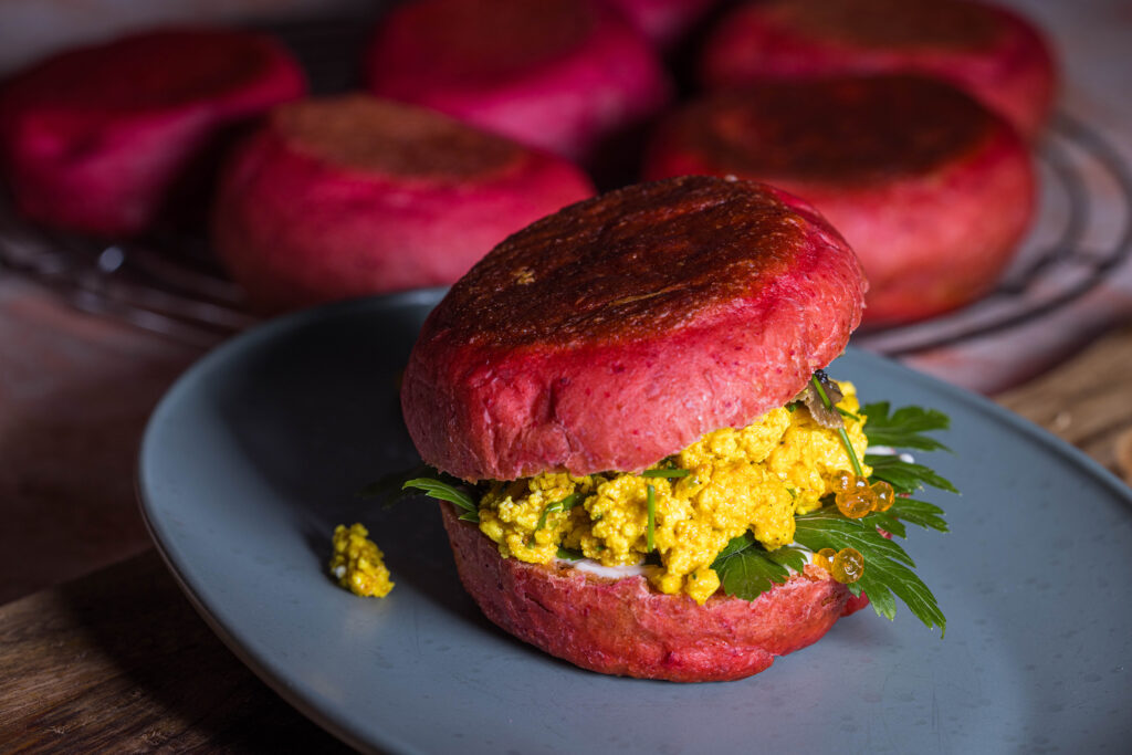 Rosa Rote Beete Pfannenbrötchen, belegt mit Scrambeld Tofu, veganem Kaviar und eingelegten Pilzen. Im Hintergrund mehr Pfannenbrötchen.