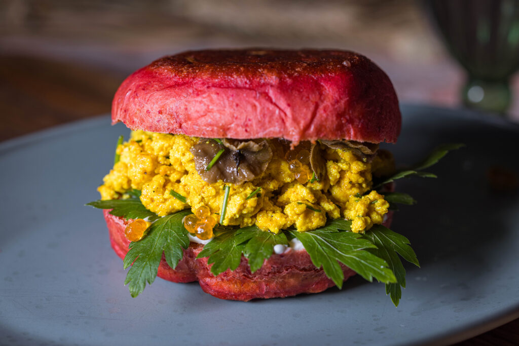 Ein Rosa Rote Beete Pfannenbrötchen, zugeklappt, belegt mit Scrambled Tofu, Mayo, eingelegten Pilzen und veganem Kaviar.