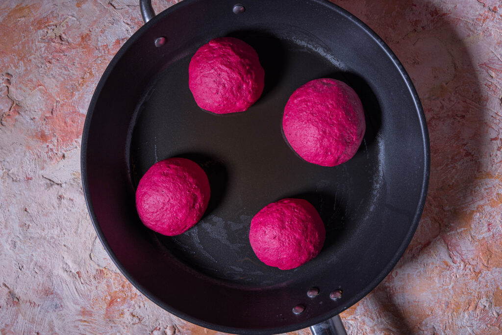 4 pinke Teigrohlinge für Pfannenbrötchen in einer Pfanne.