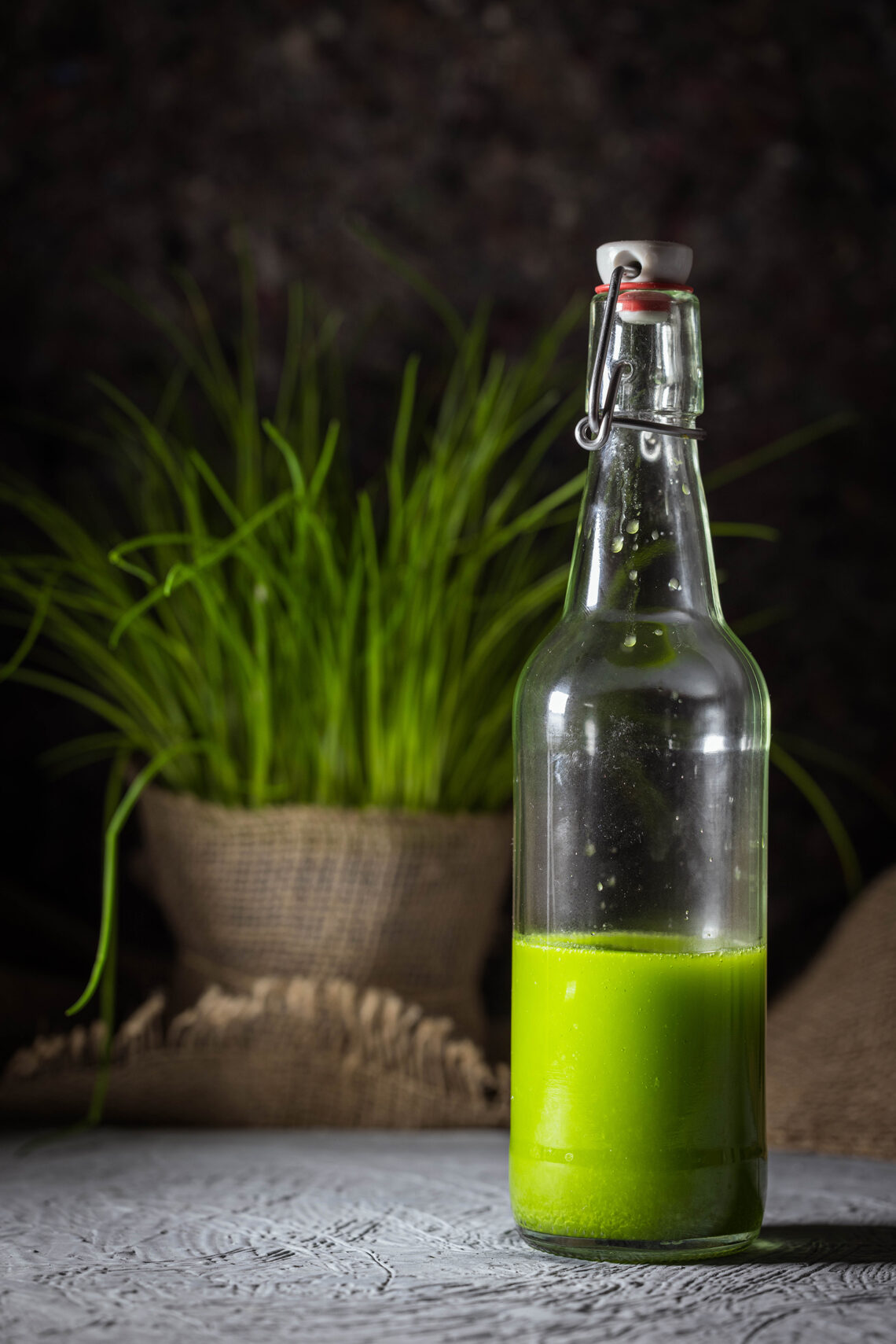 Schnittlauchöl, selbstgemacht, quietschgrün, aromatisch in einer Flasche. Im Hintergrund frischer Schnittlauch.