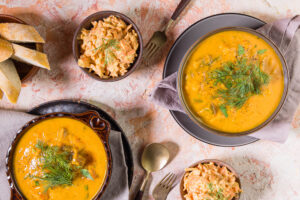 Süßkartoffel-Kokos-Suppe in zwei Schüsseln mit Brot und Salat als Beilagen.