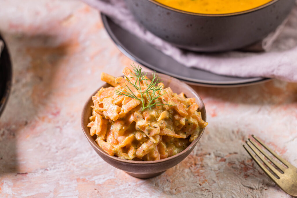 Türkischer Karottensalat in einer kleinen Schale, daneben eine Gabel und eine Schale Suppe