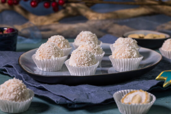 Vaffaello - Vegane Raffaello - auf einem Teller. Darum verteilt weitere Raffaellos. Einer ist angeschnittenund man sieht die Waffeln, Creme und Mandel im Inneren.