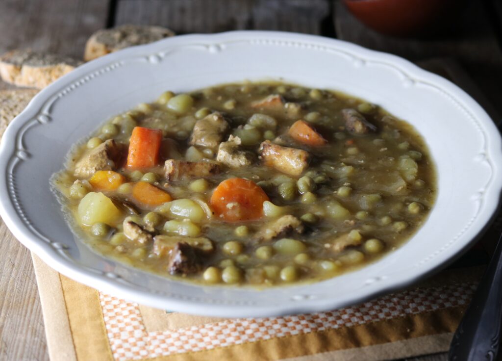 German pea stew, a hearty soup, in a bowl, with bread slices next to it.