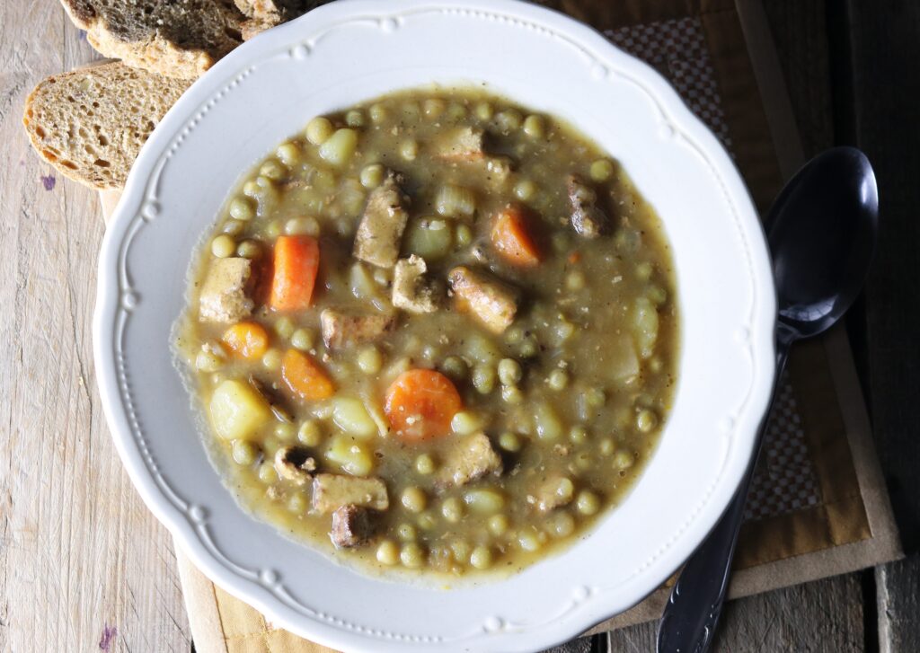 German pea stew in a bowl with a spoon and slices of bread next to it