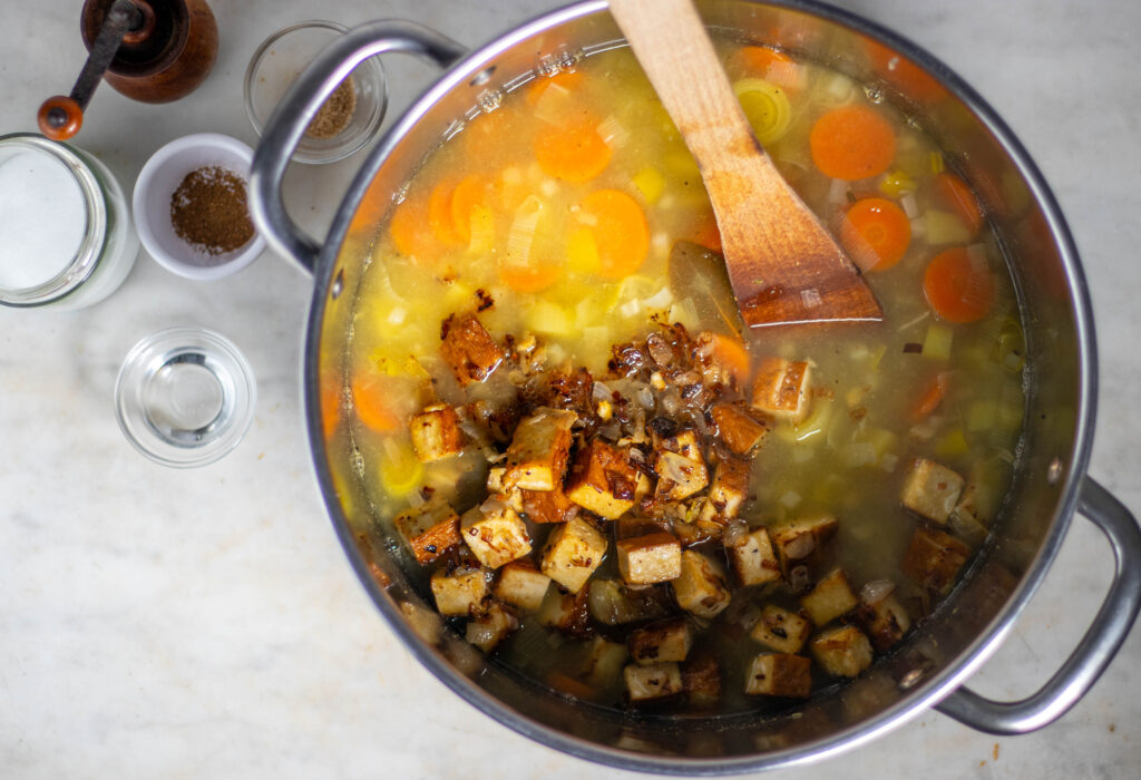 Smoked tofu and oinions are added to a pot with stew.