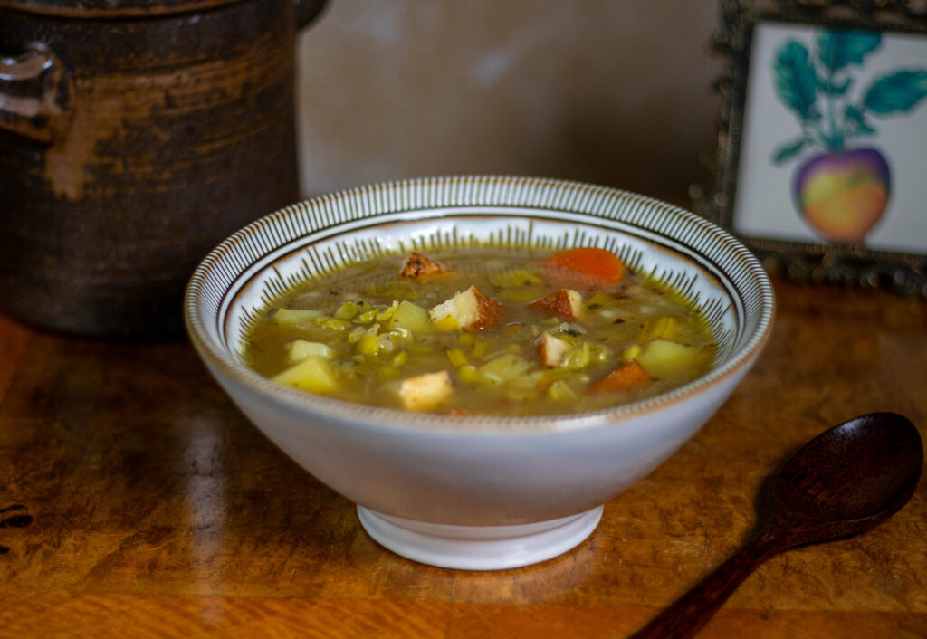 German pea stew in a bowl on an antique table with a wooden spoon next to it.