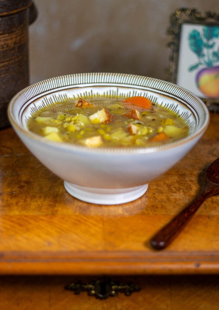 German pea stew in a bowl on an antique table with a wooden spoon next to it.